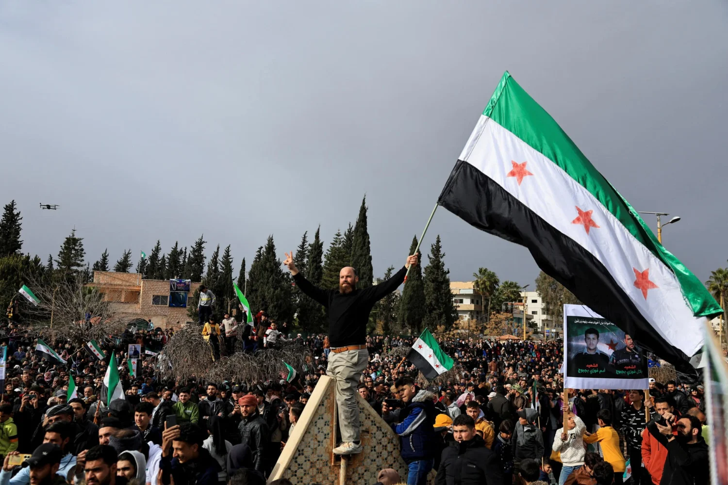A man holds the flag adopted by the new Syrian rulers, as people gather to celebrate after the ousting of Syria's Bashar al-Assad, at March 18 Square in Daraa, Syria,
